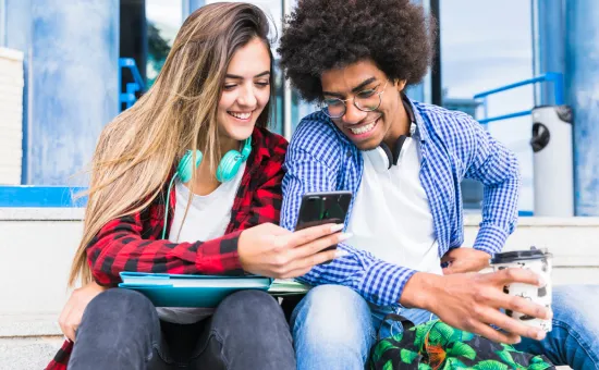 Dos estudiantes universitarios sonriendo mientras miran un teléfono celular en el campus de la Universidad César Vallejo