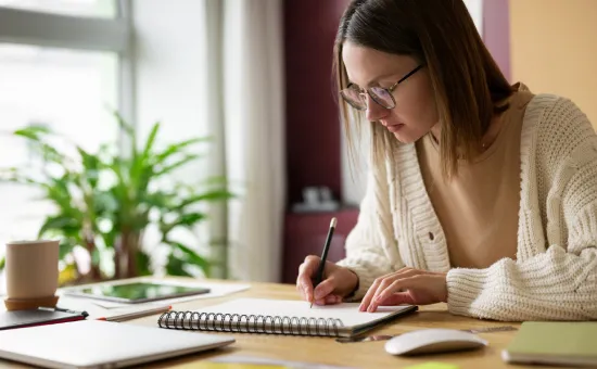 ¿Cómo el rigor académico de la UCV te prepara para destacar en el mercado laboral? Estudiante universitaria trabajando en su escritorio con una libreta y computadora